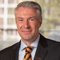 Portrait of a person wearing a suit and a striped tie, smiling in front of a blurred background.