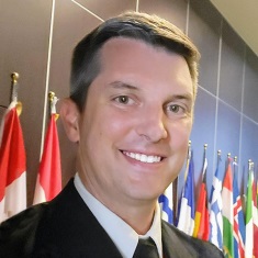 Portrait of an individual smiling in front of international flags.