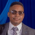 Portrait of an individual wearing glasses, a gray blazer, and a striped tie, with a blue background.