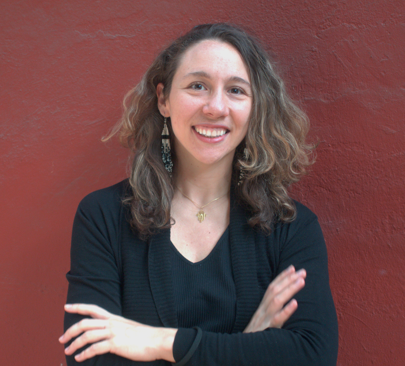 Person smiling with arms crossed, wearing a black top against a red background.