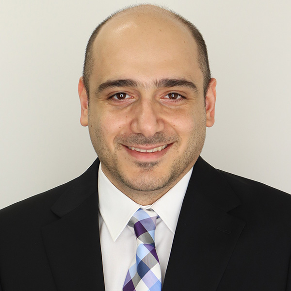 A person smiling in dark suit with blue and purple plaid tie.