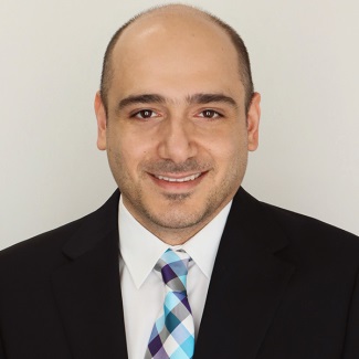 A person smiling in dark suit with blue and purple plaid tie.