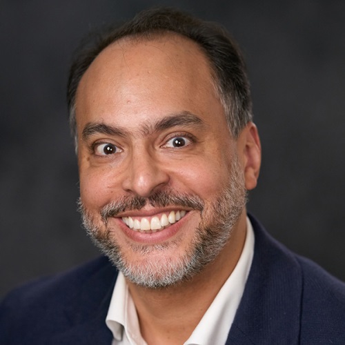 Portrait of a smiling person with short dark hair, wearing a navy blue blazer.