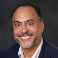 Portrait of a smiling person with short dark hair, wearing a navy blue blazer.