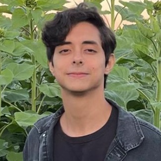 Person with a slight smile standing in front of lush green plants.