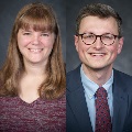 On the left, a person with shoulder-length light brown hair and bangs smiles, wearing a maroon heathered top. On the right, a person with short brown hair and glasses smiles, wearing a navy suit jacket, light blue shirt, and patterned maroon tie.