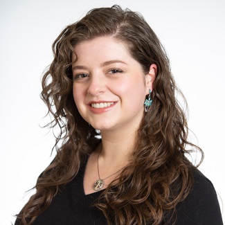 Professional headshot of a person with curly hair wearing a black top, turquoise earrings, and a necklace.