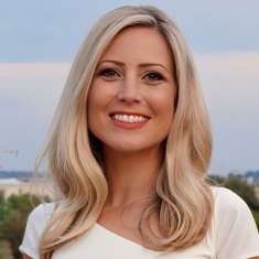 Portrait of an individual with blond hair, smiling, with a soft-focus background.
