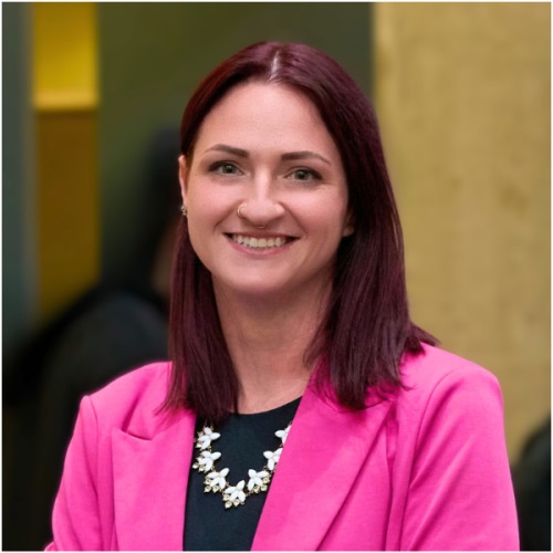 Portrait of an adult in a bright pink blazer, smiling at the camera.