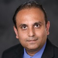 Portrait of a professional wearing a dark blue shirt, featuring a neutral background.