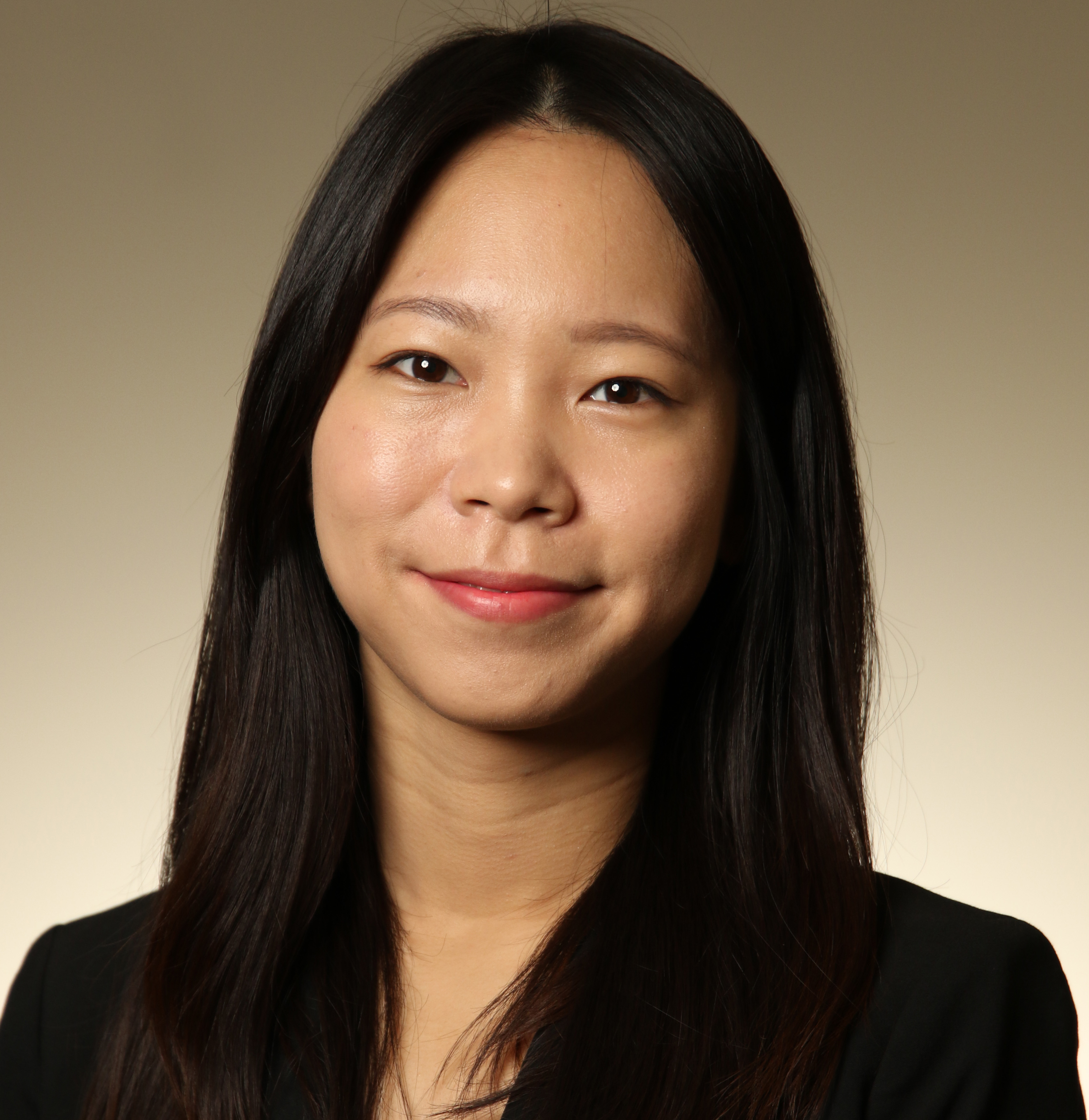 A person smiling and wearing a black blazer, set against a warm beige gradient background.