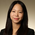A person smiling and wearing a black blazer, set against a warm beige gradient background.