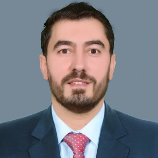 Professional headshot of a person wearing a dark blue suit, white shirt, and red patterned tie, against a grey background.