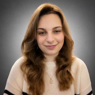 A person with long wavy hair, smiling, wearing a cream sweater.