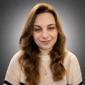 A person with long wavy hair, smiling, wearing a cream sweater.