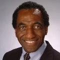 Person with dark hair wearing a suit and tie.