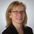 Portrait of a smiling individual with glasses, wearing a dark blazer.