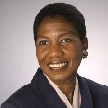 Portrait of a smiling individual wearing a dark blazer and silver earrings.