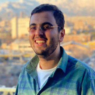 Portrait of a smiling person wearing eyeglasses and a plaid shirt, with a cityscape in the background at sunset.