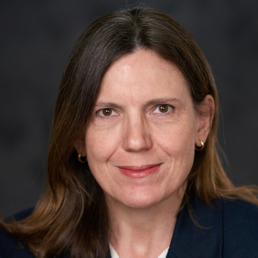 Portrait of person with dark hair smiling in a blue suit against a grey backdrop.