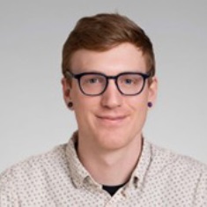 Portrait of a smiling individual wearing glasses and a dotted shirt.