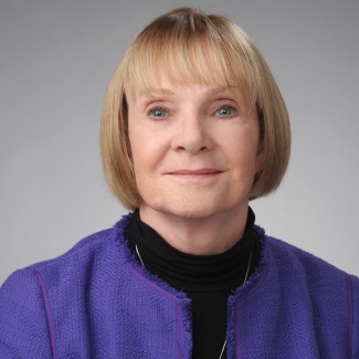 Portrait of of a person wearing a purple sweater and black turtleneck, with a neutral background.