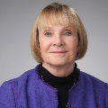 Portrait of of a person wearing a purple sweater and black turtleneck, with a neutral background.