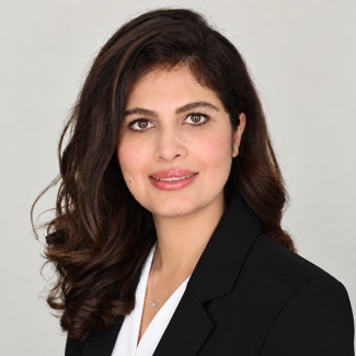 A person in dark blazer over white top with delicate necklace.
