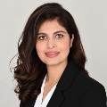 A person in dark blazer over white top with delicate necklace.
