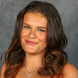 Portrait of a person smiling with long brown curly hair.