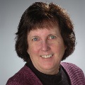 Portrait of a smiling person with short brown hair wearing a purple sweater.