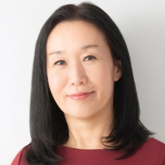 A person smiling with long, dark hair and wearing a red top.