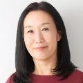 A person smiling with long, dark hair and wearing a red top.