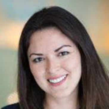 Portrait of a smiling individual with long dark hair, set against a blurred background.