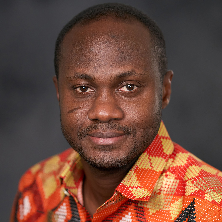 Portrait of a person wearing a brightly colored shirt, smiling gently at the camera against a dark background.