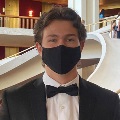Person wearing a black mask and formal attire with a bow tie, posing in front of a staircase.