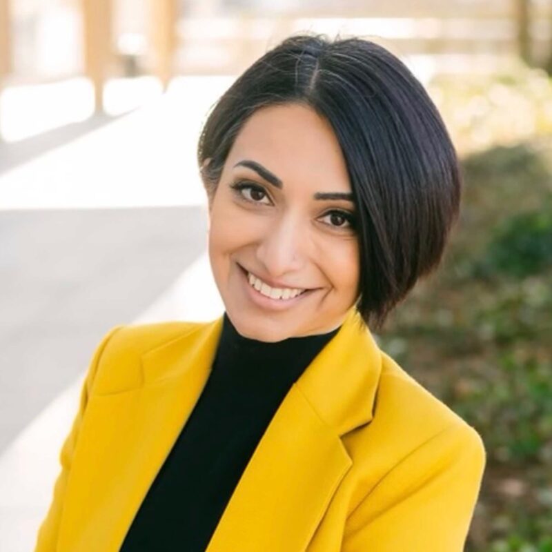 Professional portrait of a smiling individual in a yellow blazer.