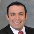 Portrait of a smiling person in a dark suit and red-striped tie.