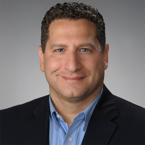 Professional headshot of a person with curly hair, wearing a dark blazer and a blue shirt, smiling at the camera.