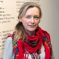 A person wearing a red scarf stands in front of a wall with text.