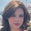 Close-up portrait of a person with short wavy hair, against a blurred background.