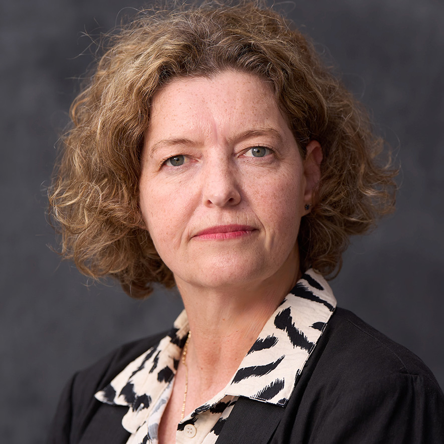Portrait of person against a dark backdrop, wearing a black and white blouse.