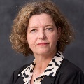 Portrait of person against a dark backdrop, wearing a black and white blouse.