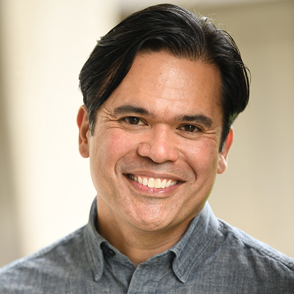 Close-up portrait of a smiling person with short black hair, wearing a gray shirt.