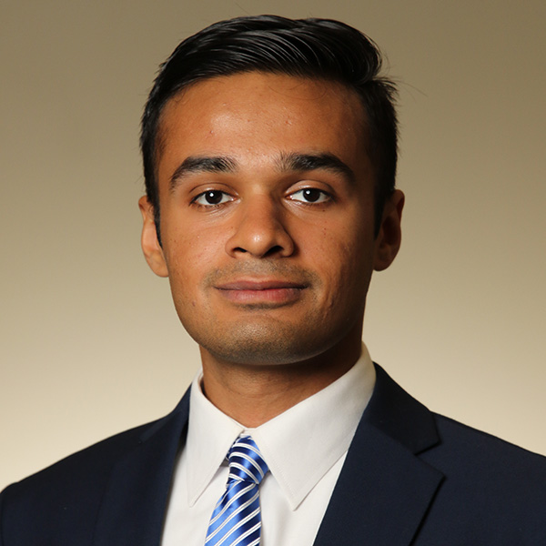 A person wearing a navy suit, white dress shirt, and a blue and white striped tie, set against a neutral beige background