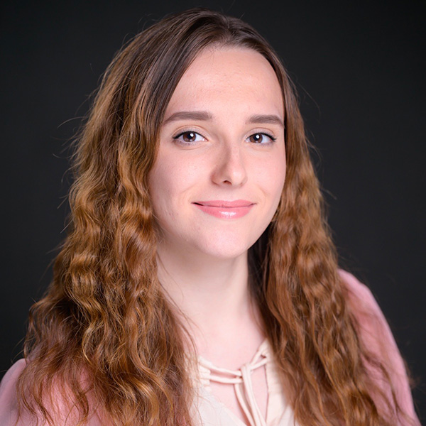 Professional portrait of a person with brown eyes and long reddish brown hair, wearing a pink top.