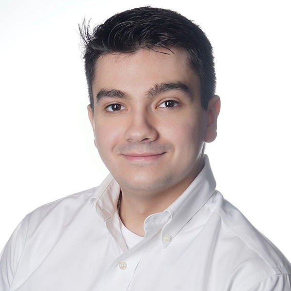 A person smiling, with dark hair, wearing a white button-up shirt.