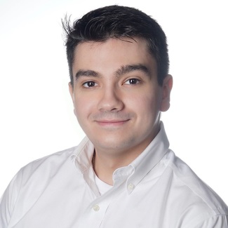 A person smiling, with dark hair, wearing a white button-up shirt.
