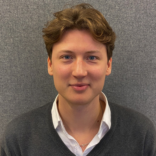 Portrait of a person with shoulder-length brown hair, wearing a white shirt and grey sweater.