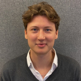 Portrait of a person with shoulder-length brown hair, wearing a white shirt and grey sweater.